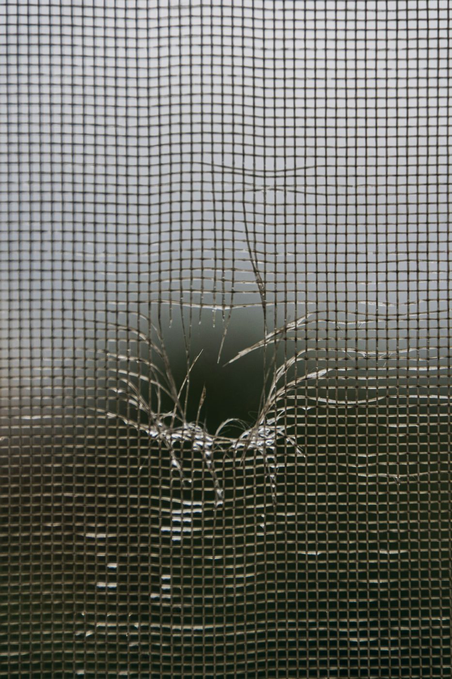 Close-up of a torn window screen mesh in need of repair